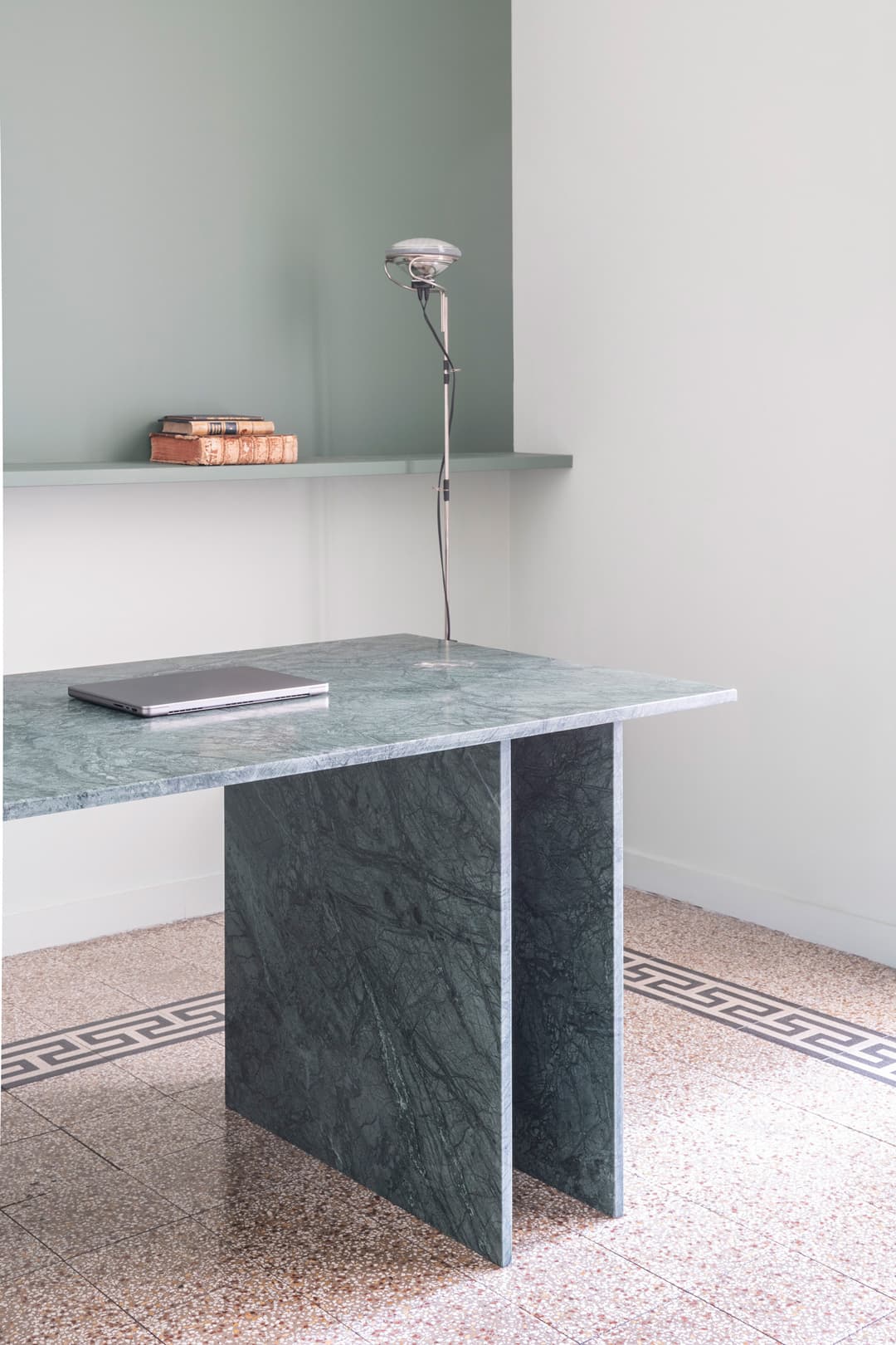 Modern room with a green marble table and books on a shelf. The floor has a geometric border pattern.