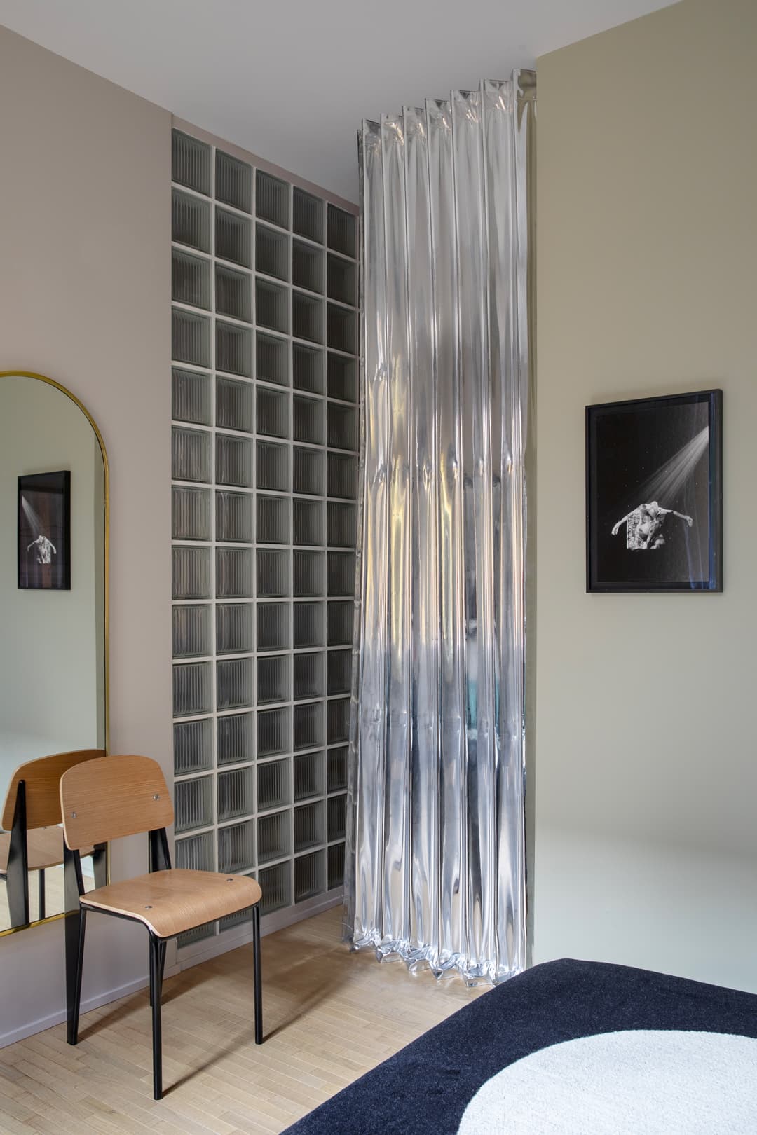 Modern room with a wooden chair, glass block wall, silver curtain, and framed black-and-white photo. Neutral walls and wooden floor.