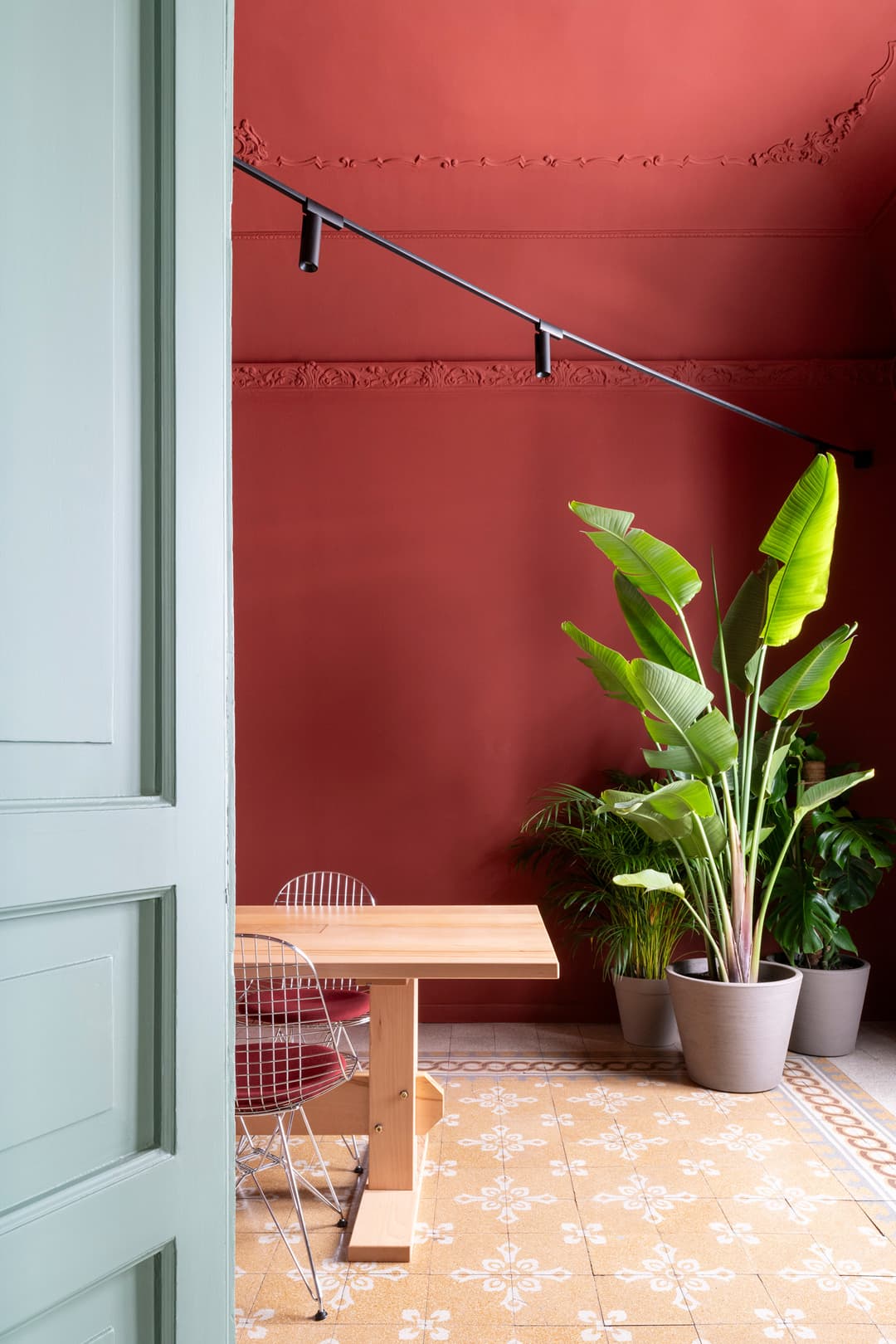 Room with red walls, a wooden table, wire chairs, and potted plants.