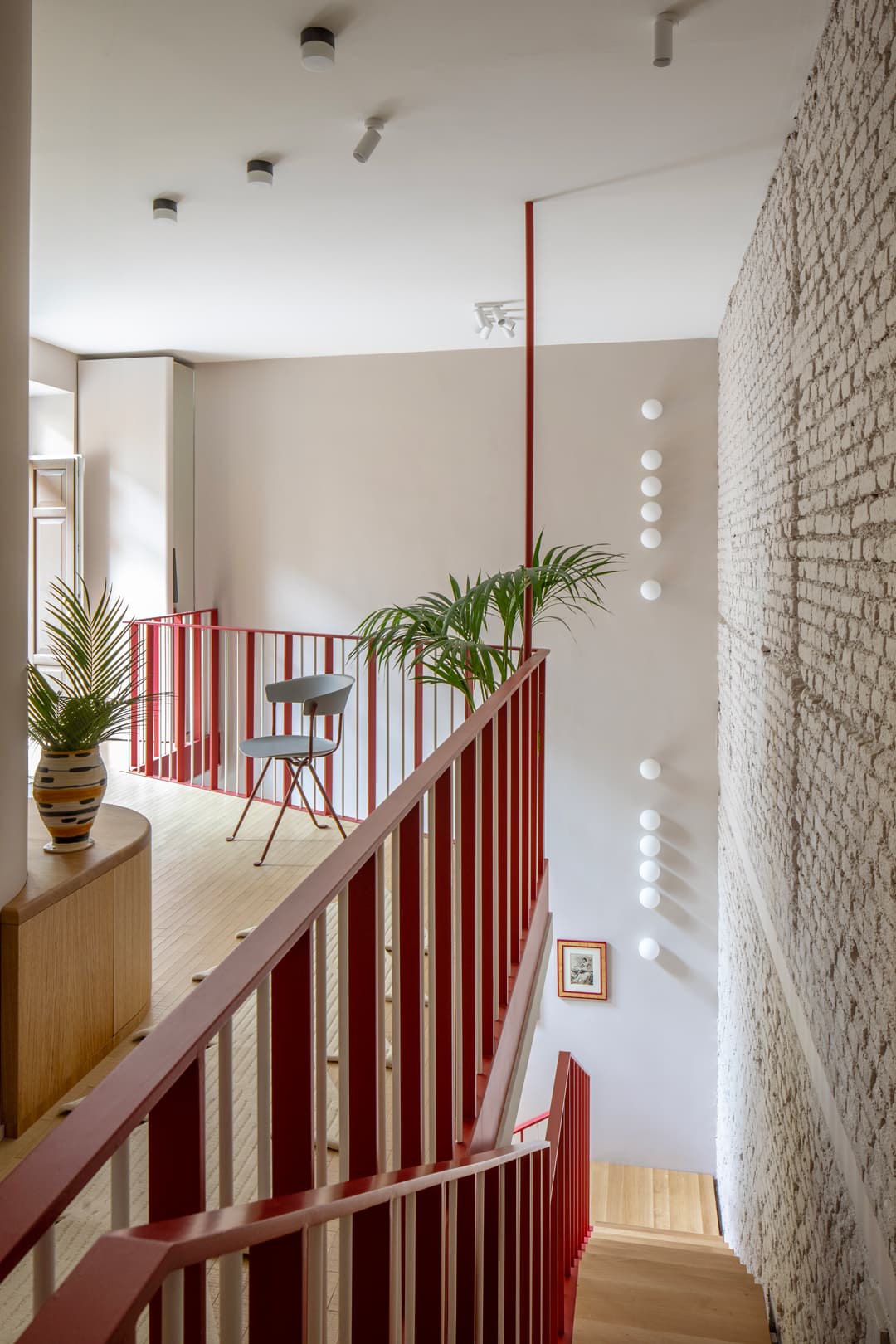 Modern interior with staircase, exposed brick wall, and wooden flooring. A chair and potted plants add to the minimalist decor.