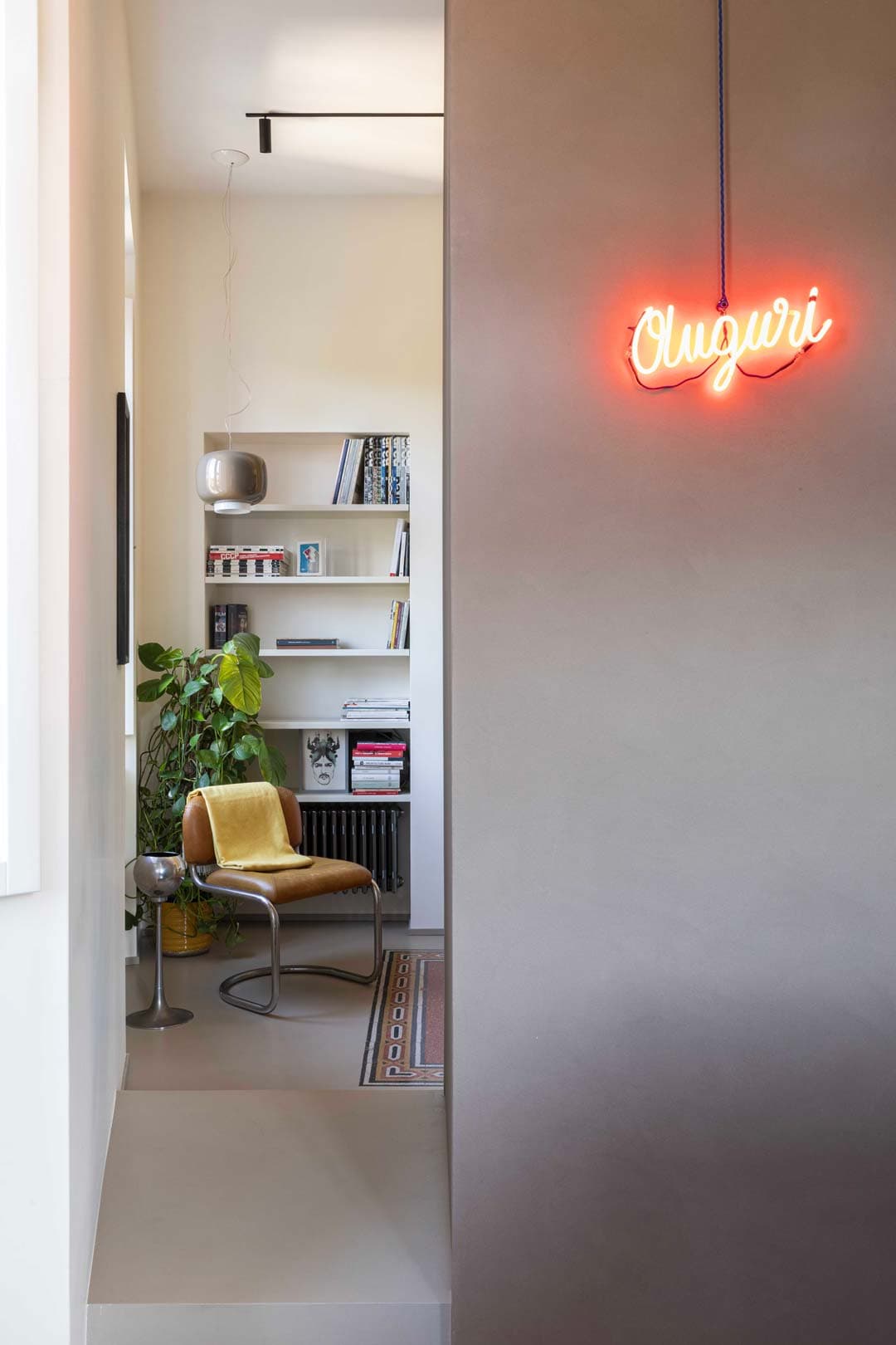 Modern interior with a yellow chair, potted plant, and shelves. Orange neon on a gray wall.