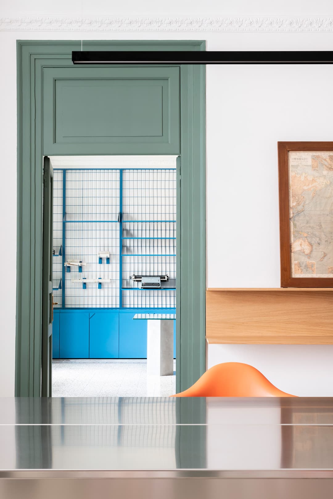 A modern interior with a green door frame, blue shelves, an orange chair, and a wooden accent wall.