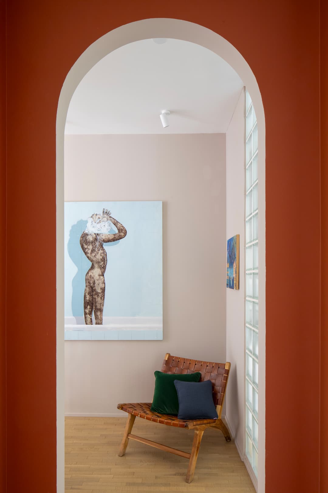 Arched doorway view of a room with a wooden chair and colorful cushions, and a large painting of a silhouetted figure on the wall.