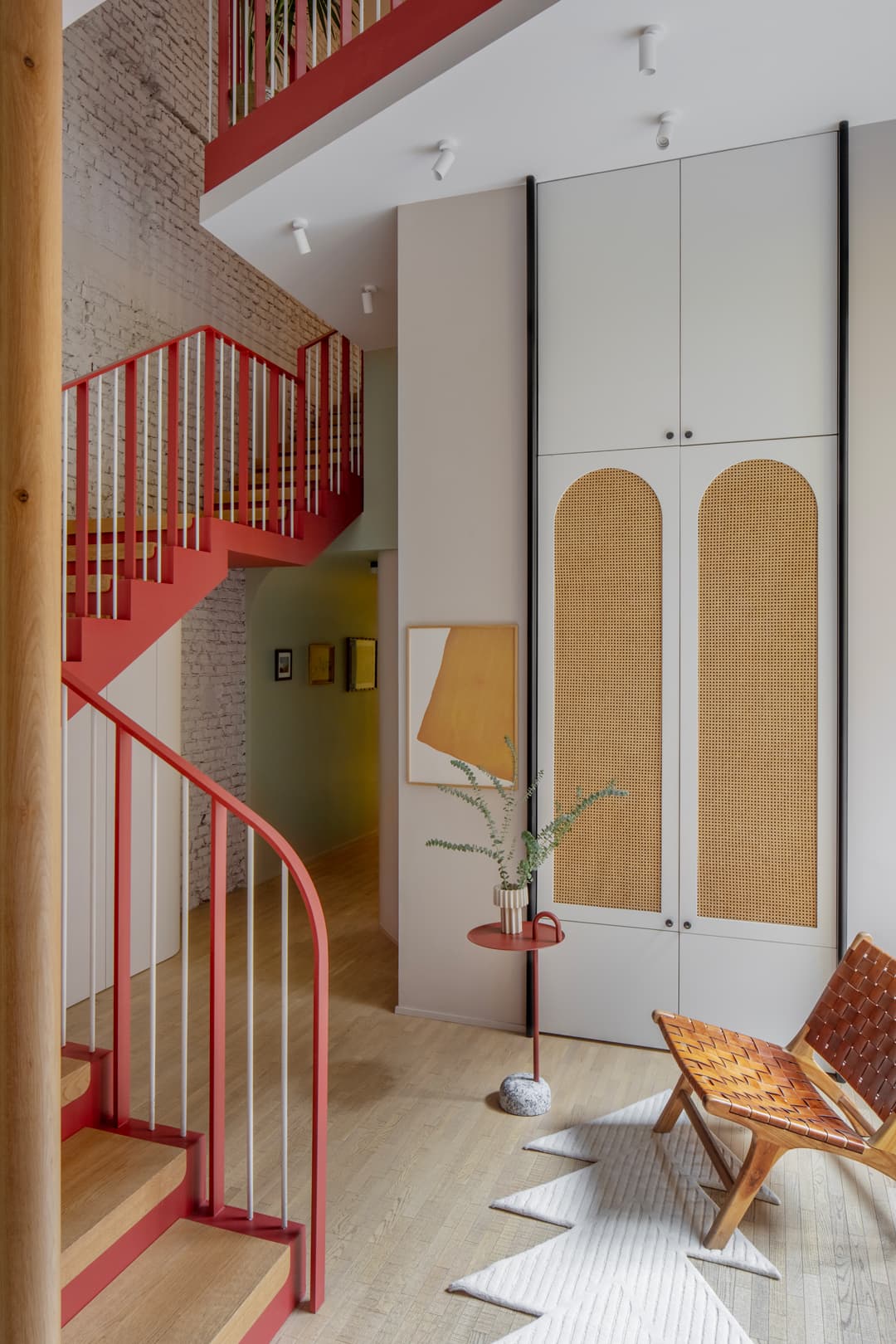 Modern interior with a red spiral staircase, abstract art, and a geometric rug on a wooden floor.