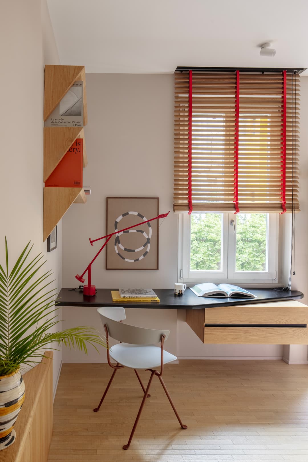 Modern home office with a wooden desk, red lamp, chair, and window with blinds.