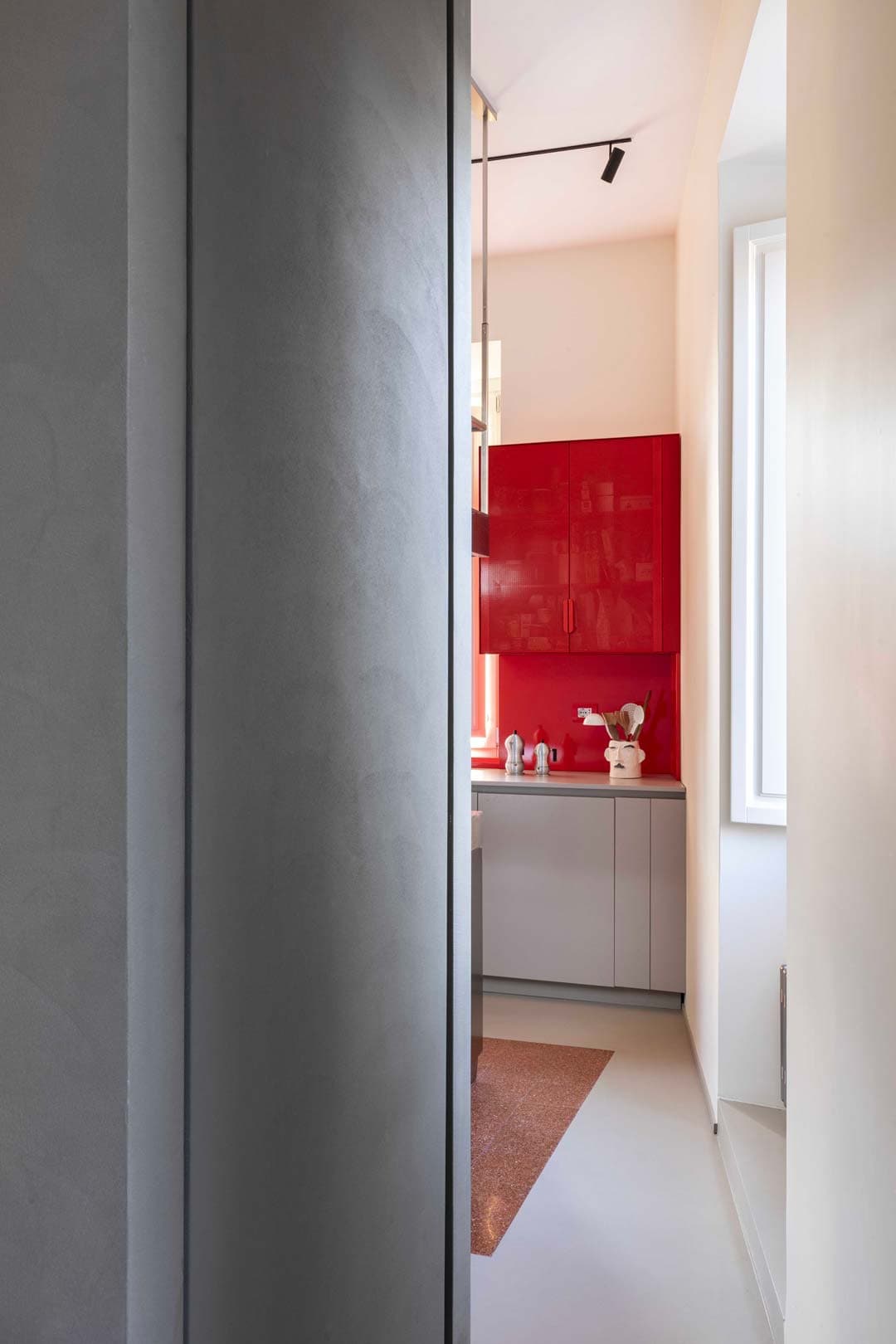 Narrow view of a modern kitchen with red cabinets and a small window allowing natural light in.