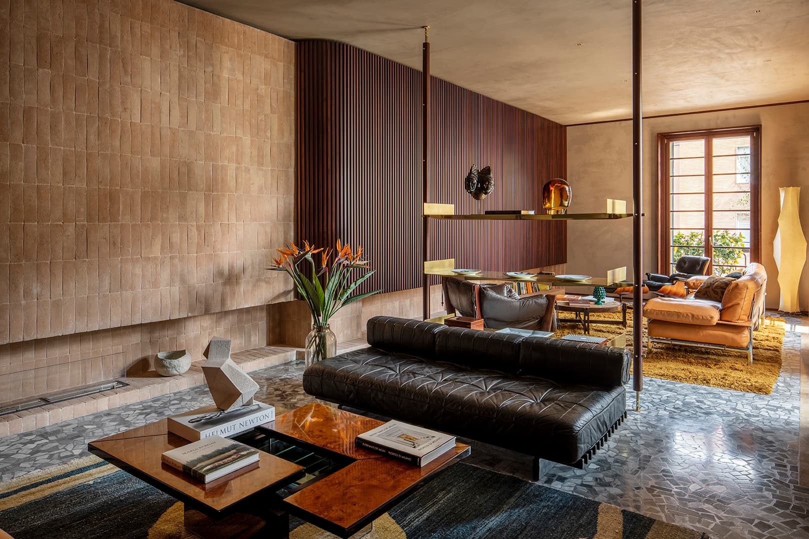 Stylish living room with modern furniture, a black leather sofa, wooden accents, a vase of flowers, and large windows letting in natural light.