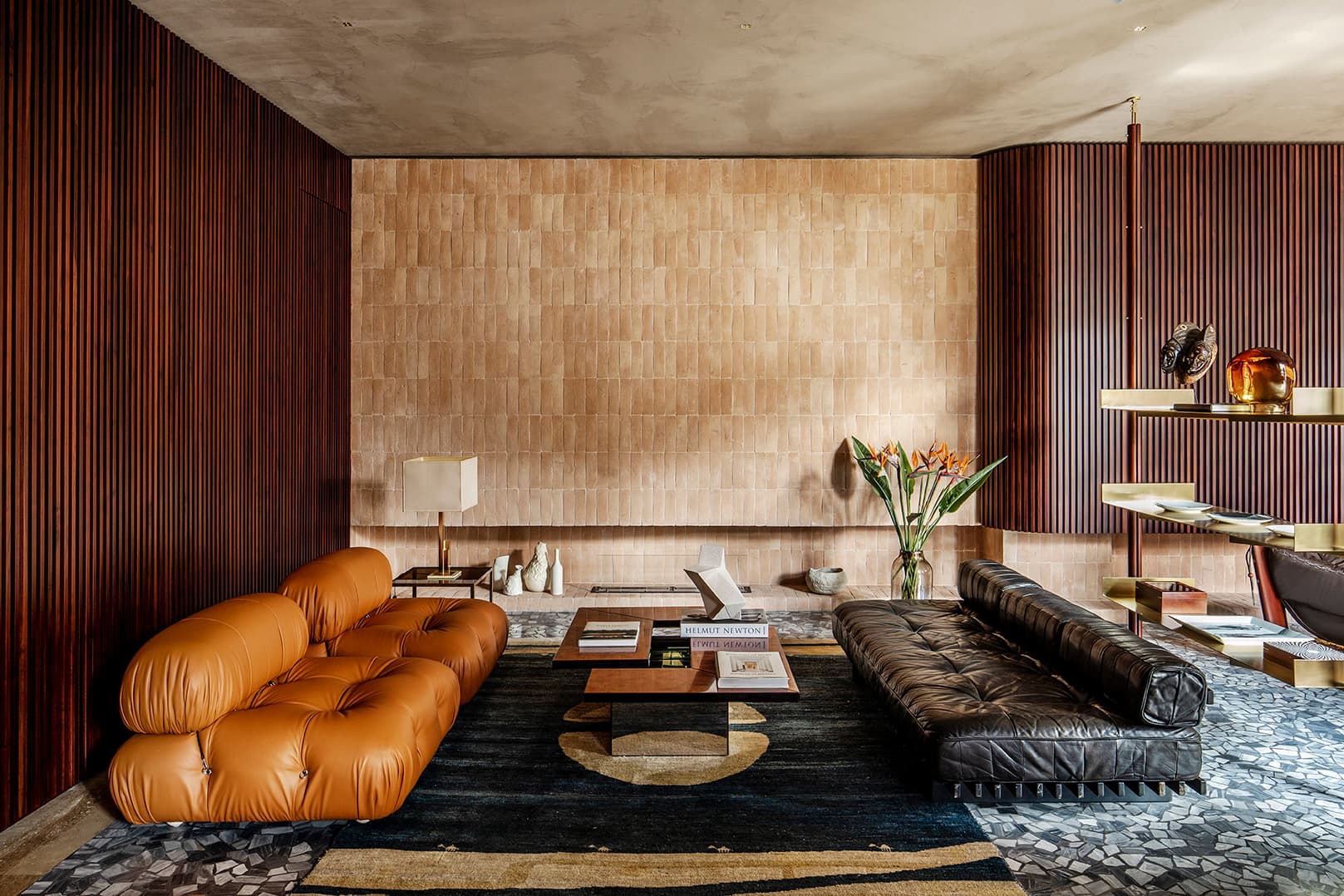 Modern living room with brown and black sofas, and geometric floor. Wooden panel walls and minimalist decor.