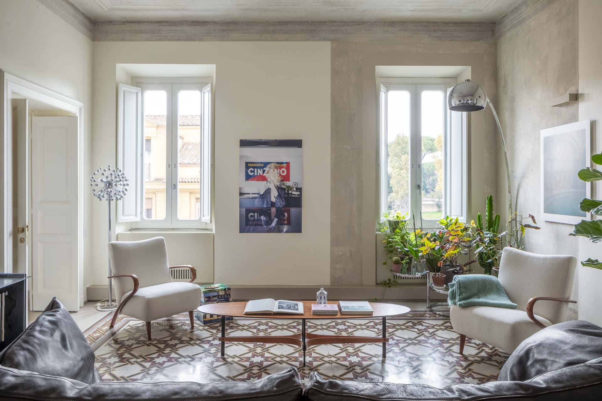 Bright living room with patterned tile floor, two white armchairs and a coffee table. Wall art and a floor lamp add decor.