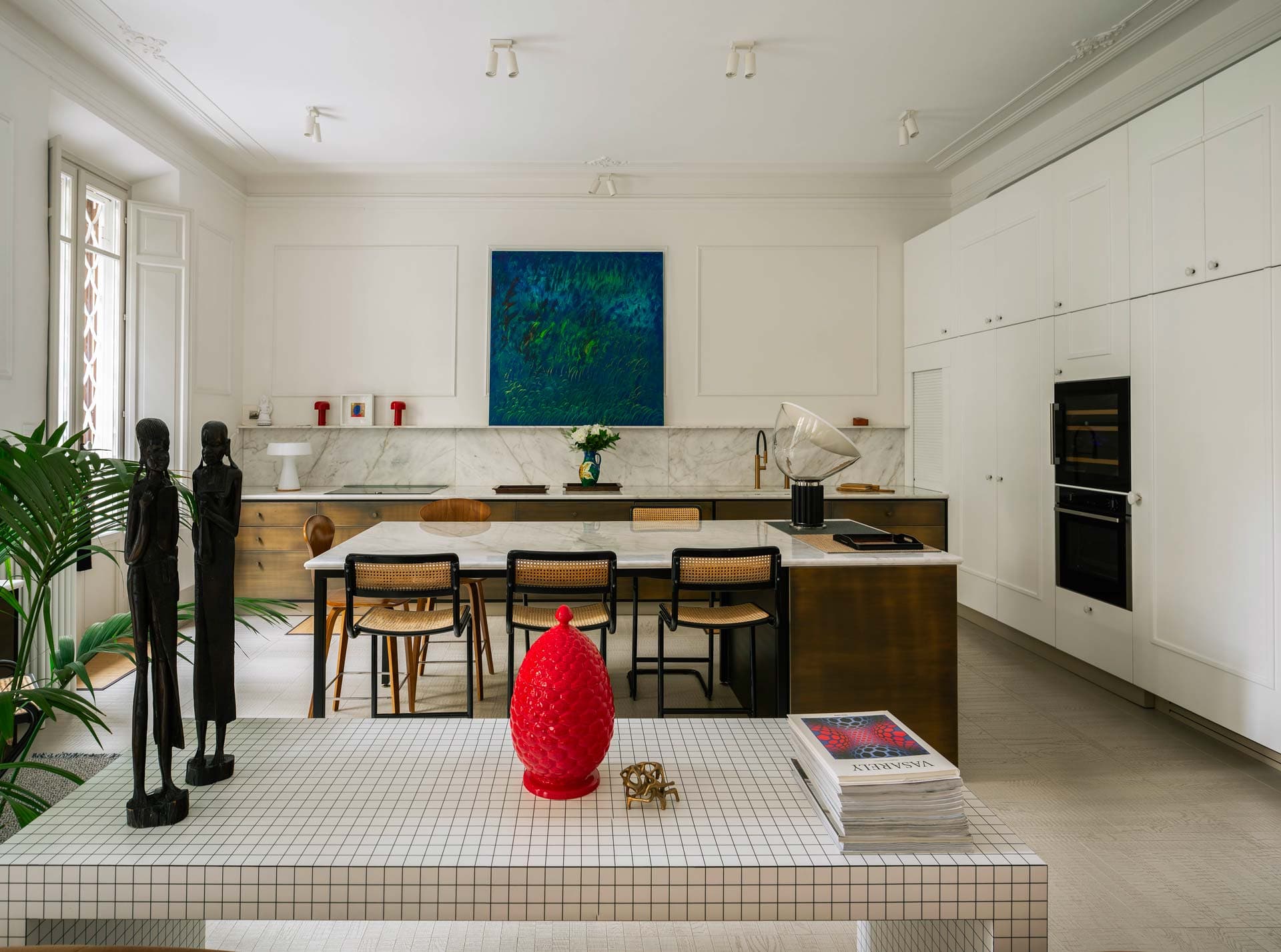 Modern kitchen with white cabinets, a marble backsplash, and a central island with wooden chairs. Art pieces and decor enhance the space.