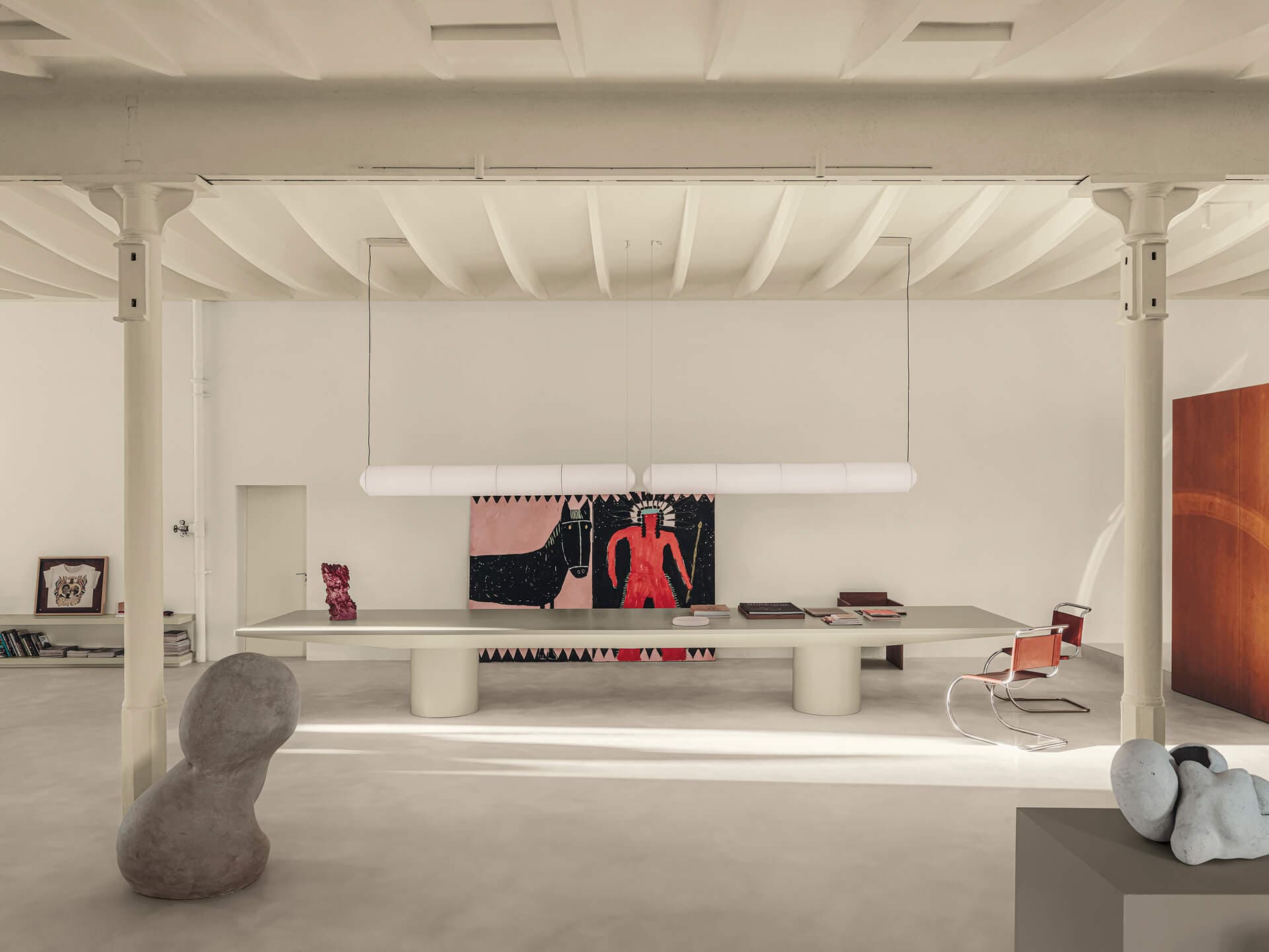 Spacious modern art studio with large table, abstract sculptures, and colorful artwork on walls under a high, white ceiling.