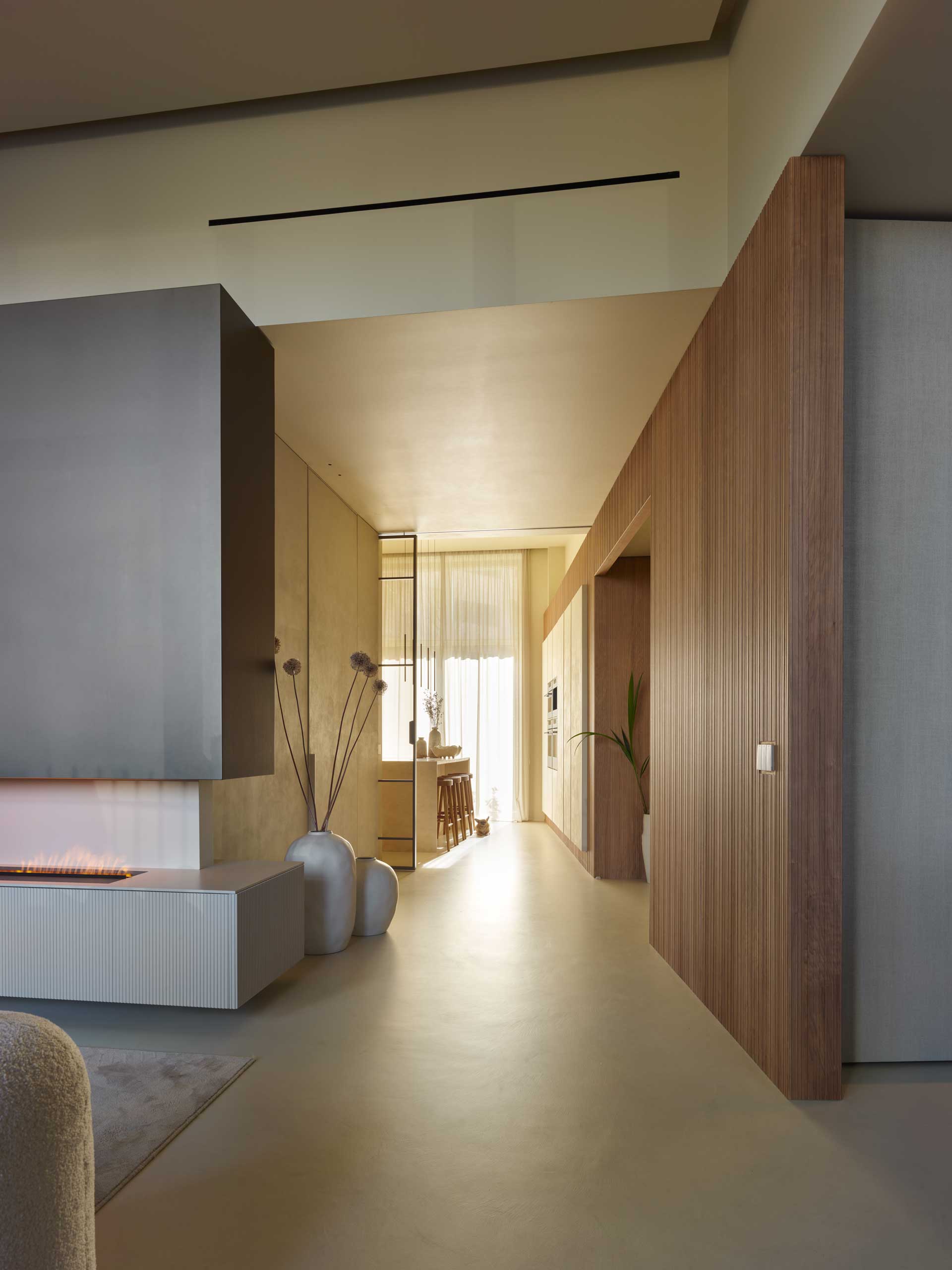 Modern interior with minimalist design, featuring a fireplace, wooden paneling, tall vases, and natural light streaming through sheer curtains.