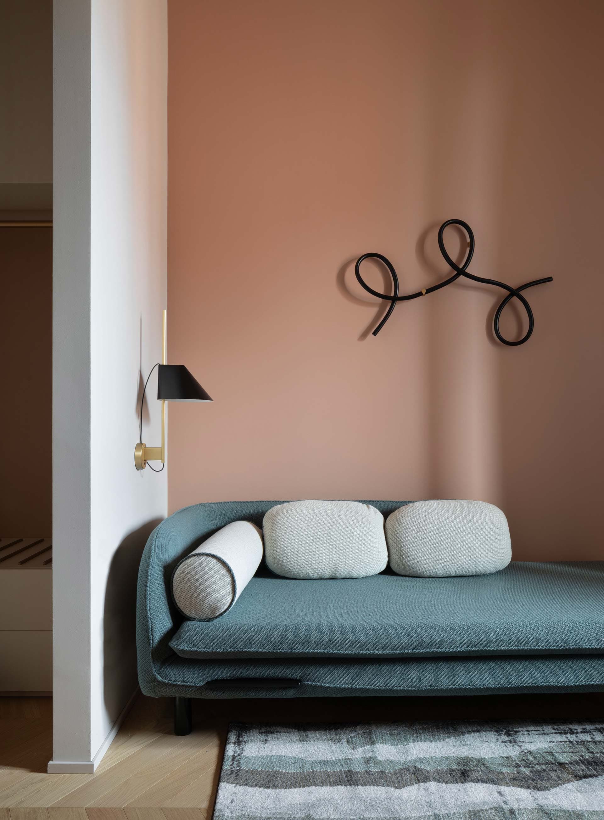 Modern living room with a sofa, white cushions, abstract wall art, and a black wall lamp against a peach-colored wall.