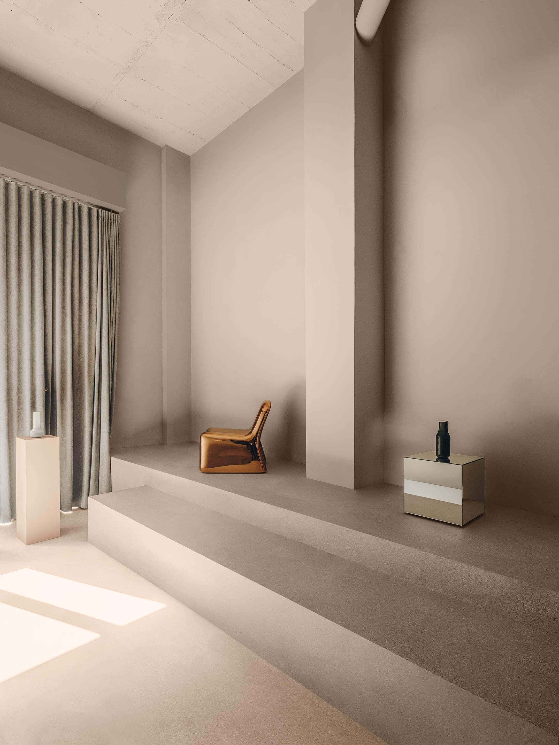 Minimalist room with neutral tones, featuring a modern chair, a small table with a vase, and floor-to-ceiling curtains.