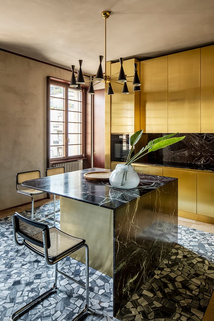Modern kitchen with gold cabinets, black marble island and geometric floor tiles. A window provides natural light.