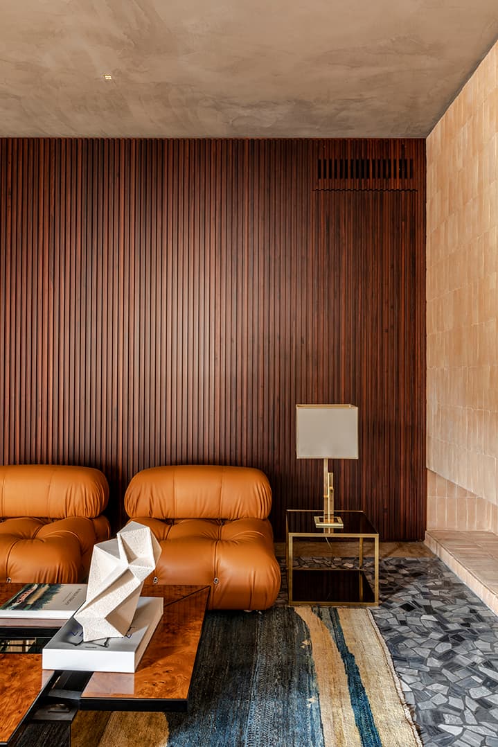 Modern living room with brown leather sofas, a geometric sculpture, a gold lamp on a side table, and a textured wood-paneled wall.